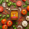 A jar of Cholula Original Hot Salsa is surrounded by fresh ingredients like tomatoes, onions, garlic, jalapeños, cilantro, and dried chili peppers.