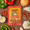 A Cholula Original Fajita Seasoning Mix packet is surrounded by fresh ingredients like peppers, onions, and garlic.
