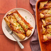 A plate of enchiladas with melted cheese and a fork next to a baking dish of more enchiladas.