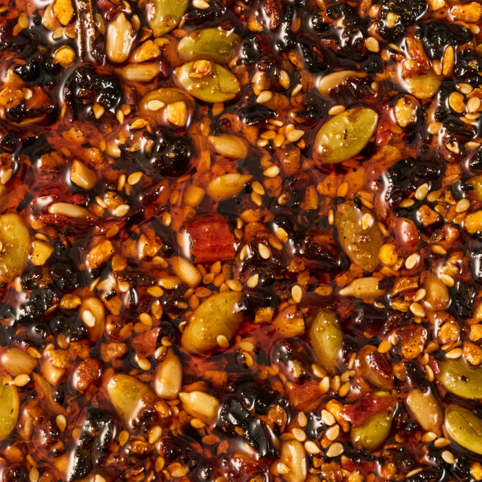 A close-up shot reveals a dense mixture of seeds nuts and dried fruits bound together by a glossy dark syrup creating a visually appealing and textured food composition.