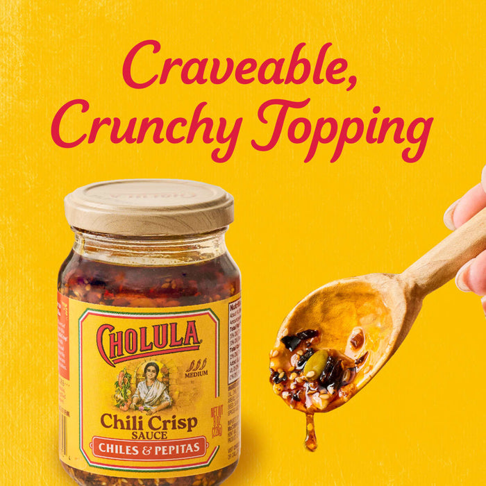 A jar of Cholula Chili Crisp Sauce is displayed next to a wooden spoon holding the sauce with the text Craveable Crunchy Topping above.