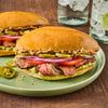 A delicious-looking steak sandwich with avocado tomato red onion and jalapeA?os is served on a green plate.