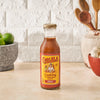 A bottle of Cholula Cooking &amp; Simmer Sauce Birria is displayed on a kitchen counter with limes garlic and wooden spoons.