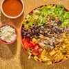 A vibrant and appetizing salad featuring grilled chicken black beans avocado corn tomatoes tortilla chips and jalapenos served with a side of dressing and crumbled cheese.