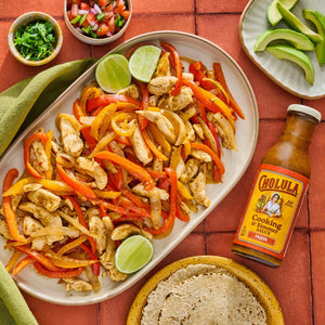 A plate of chicken fajitas with Cholula Cooking &amp; Simmer Sauce accompanied by tortillas avocado slices pico de gallo and cilantro.