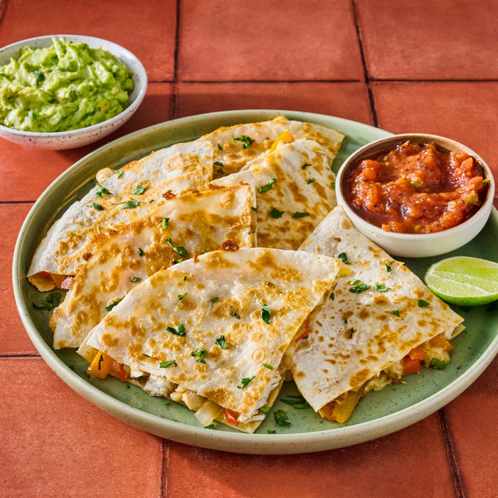 A plate of quesadillas is served with guacamole salsa and a lime wedge.