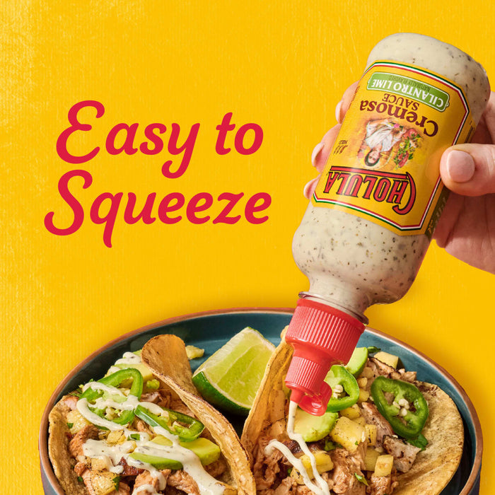 A hand squeezes Cholula Cremosa Cilantro Lime sauce onto tacos filled with meat pineapple and jalapeA?os.