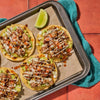 A tray of delicious tostadas topped with guacamole meat and various toppings accompanied by a lime wedge.