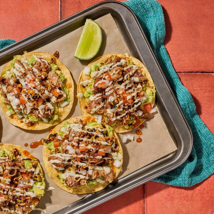 A tray of delicious tostadas topped with guacamole meat and various toppings accompanied by a lime wedge.