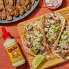 Cholula Cremosa Sauce Cilantro Lime is featured alongside a wooden board with three tacos filled with steak guacamole radishes onions and sauce.