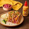 A plate of tacos with Cholula Cremosa Chipotle sauce, accompanied by a side of slaw and lime wedges.