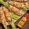 A plate of Mexican street corn or elote topped with Cholula Cremosa Chipotle sauce and lime wedges.