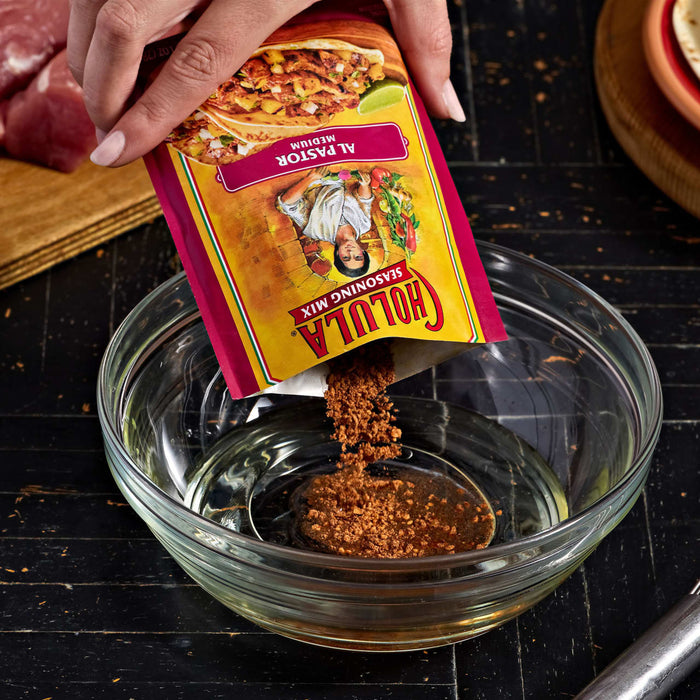A hand pours a packet of Goya Adobo seasoning into a glass bowl.