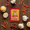 A packet of GOYA Sazón seasoning is surrounded by garlic, onions, and red chili peppers on a wooden surface.