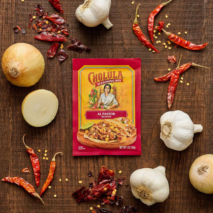 A packet of GOYA Sazón seasoning is surrounded by garlic, onions, and red chili peppers on a wooden surface.