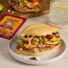 A delicious Cemitas sandwich featuring Cacique brand products is displayed on a plate next to a packet of Cacique Refried Beans.