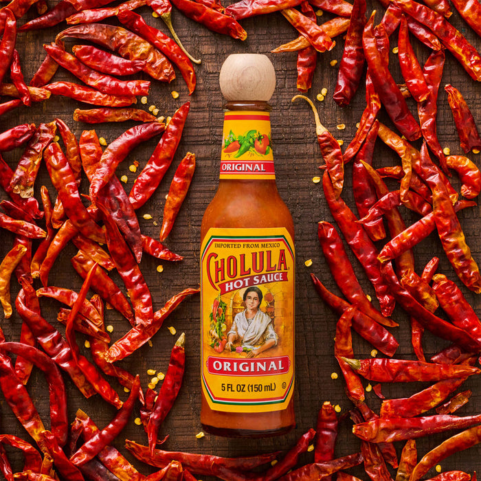 A bottle of Cholula Original Hot Sauce surrounded by dried red chili peppers.