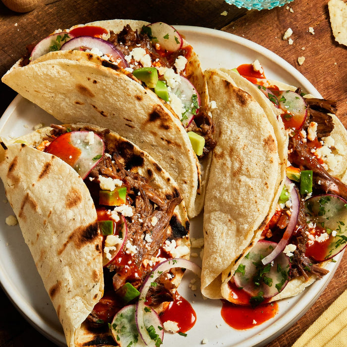 Three tacos filled with meat, cheese, and vegetables on a white plate.