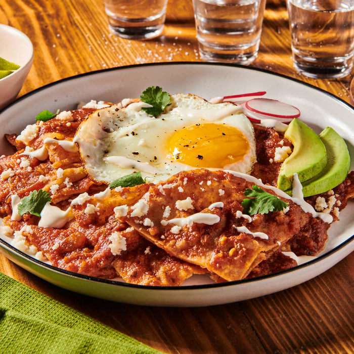 A plate of chilaquiles with a fried egg, avocado, and crema.