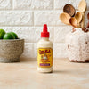 A bottle of Cholula Creamy Chipotle sauce sits on a countertop next to limes and kitchen utensils.