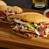 A delicious steak sandwich with lettuce, tomato, and creamy sauce is presented on a wooden board.