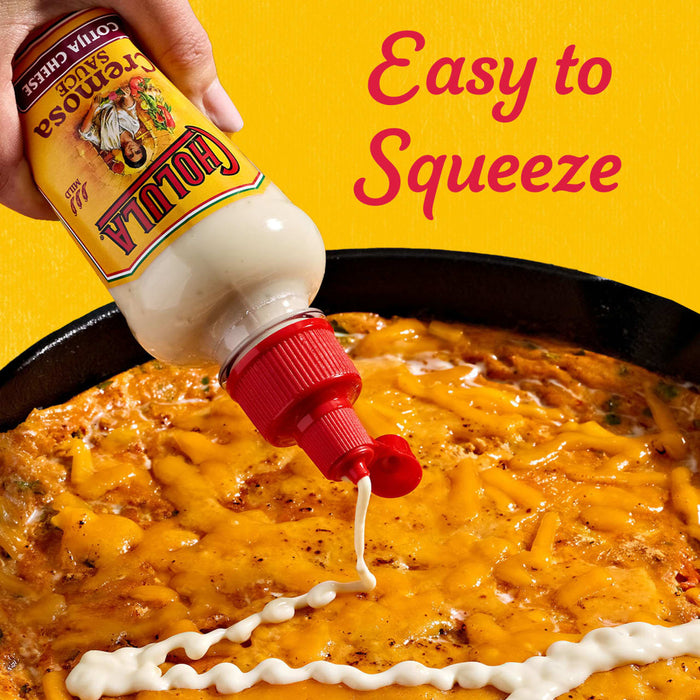 A hand squeezes a bottle of Cholula Creamy Jalapeño sauce over a cheesy dish, highlighting its easy-to-squeeze feature.