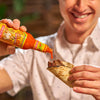 A smiling person squeezes Cholula Original Hot Sauce onto a taco filled with meat.