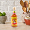 A bottle of Cholula Original Hot Sauce stands on a kitchen counter next to limes, garlic, and wooden utensils.