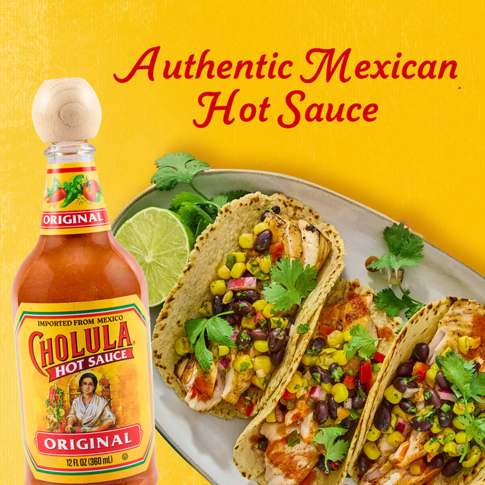 A bottle of Cholula Original Hot Sauce is prominently displayed next to a plate of three delicious chicken tacos garnished with corn and black bean salsa and fresh cilantro, set against a bright yellow background.