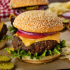 A close-up of a cheeseburger with lettuce, tomato, onion, and a sesame seed bun.