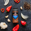 A bottle of McCormick Montreal Steak Spice is surrounded by fresh ingredients like peppers, onions, garlic, and peppercorns.