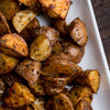 A close-up shot of roasted potatoes seasoned with herbs in a white serving dish.