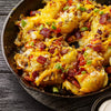 A close-up of a skillet filled with loaded baked potatoes topped with cheese, bacon, and chives.
