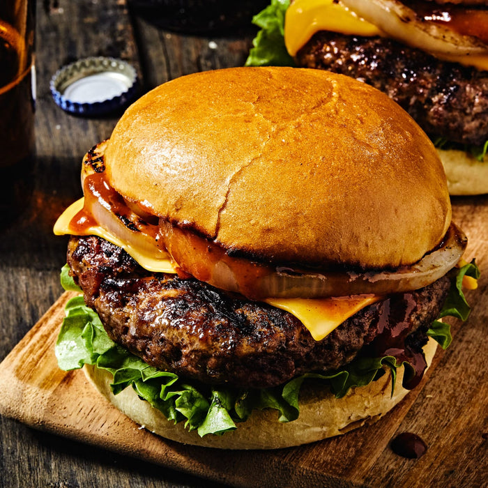 A close-up of a juicy cheeseburger with lettuce and onion on a wooden cutting board.