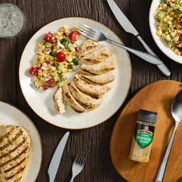 A plate of sliced grilled chicken and corn salad is displayed with a bottle of McCormick Grill Mates Montreal Chicken Seasoning.