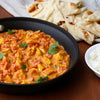A skillet of chicken tikka masala with naan bread and rice on the side.