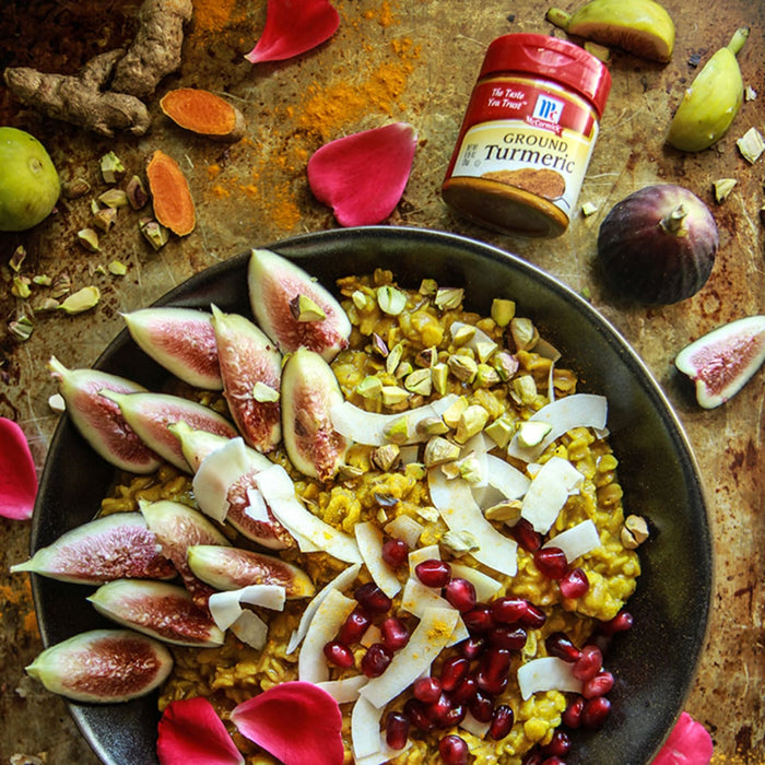 A bowl of turmeric oatmeal topped with figs, pistachios, coconut flakes, and pomegranate seeds, with a jar of McCormick Ground Turmeric in the background.