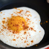 A fried egg with spices in a black pan.