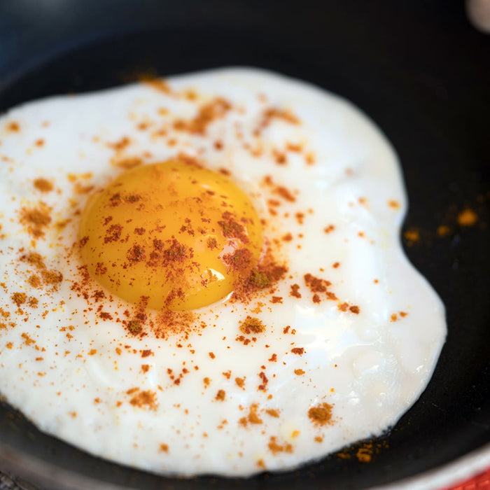 A fried egg with spices in a black pan.