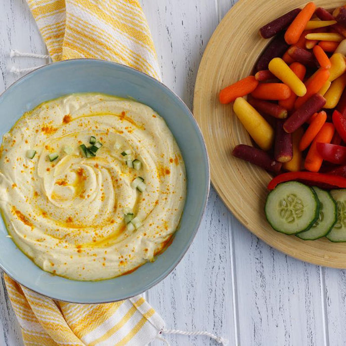 A bowl of hummus with cucumber and a plate of carrots, peppers, and cucumbers.
