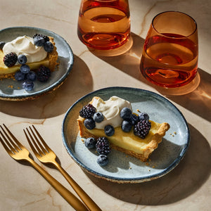 A visually appealing arrangement of key lime pie slices topped with whipped cream and fresh berries, accompanied by two glasses of amber liquid, suggesting a refreshing dessert and beverage pairing.