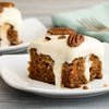 A close-up of a slice of carrot cake with cream cheese frosting and pecans.