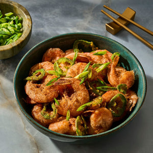 A bowl of stir-fried shrimp with sliced green peppers is presented alongside chopsticks, showcasing a delicious Asian-inspired dish.