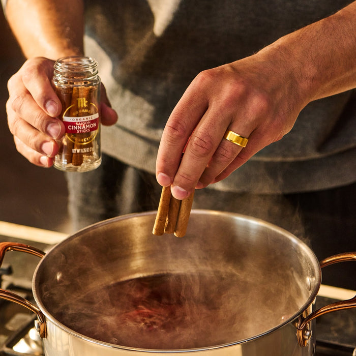 A person adds cinnamon sticks to a pot, possibly for a recipe or beverage.