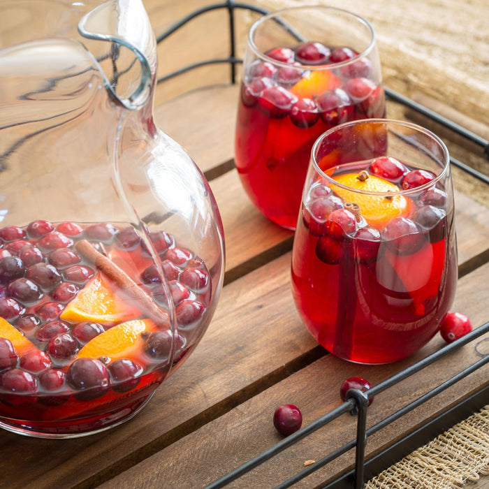 A pitcher and two glasses of cranberry juice with orange slices and cinnamon sticks.