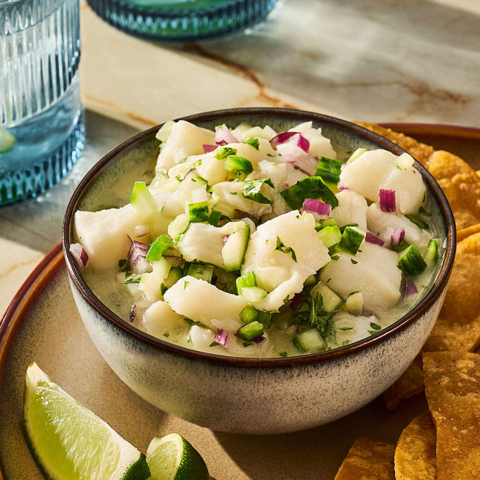 A bowl of fresh ceviche with lime wedges and tortilla chips is presented on a plate.