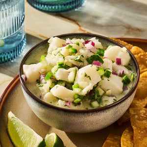 A bowl of fresh ceviche with lime wedges and tortilla chips is presented on a plate.