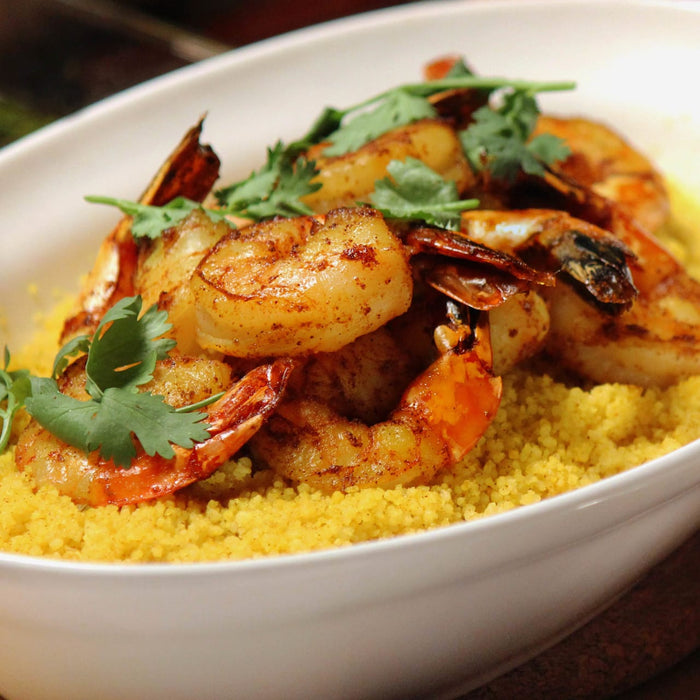 A bowl of couscous topped with grilled shrimp and cilantro.