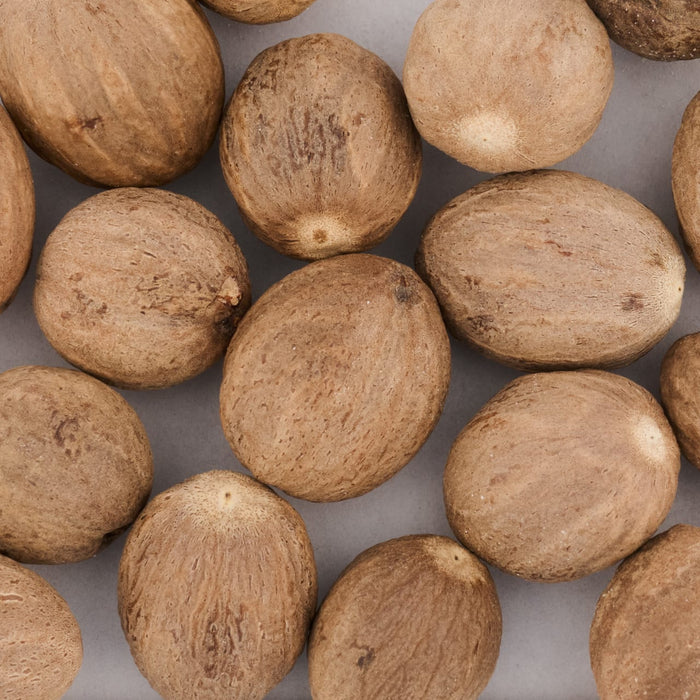 A close-up shows a collection of whole nutmeg seeds, highlighting their rough texture and brown color.