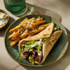 A plate with a gyro sandwich, fries topped with feta cheese, and a side of tzatziki sauce.